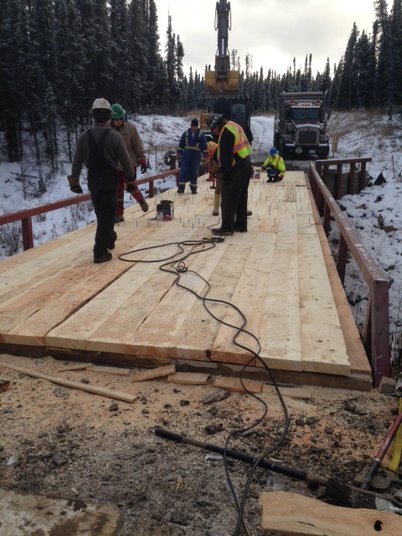 wooden bridge in the forest with construction workers building and standing on it